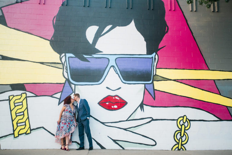 curly haired woman kissing a redheaded man in front of large female mural in the Funk Zone of Santa Barbara