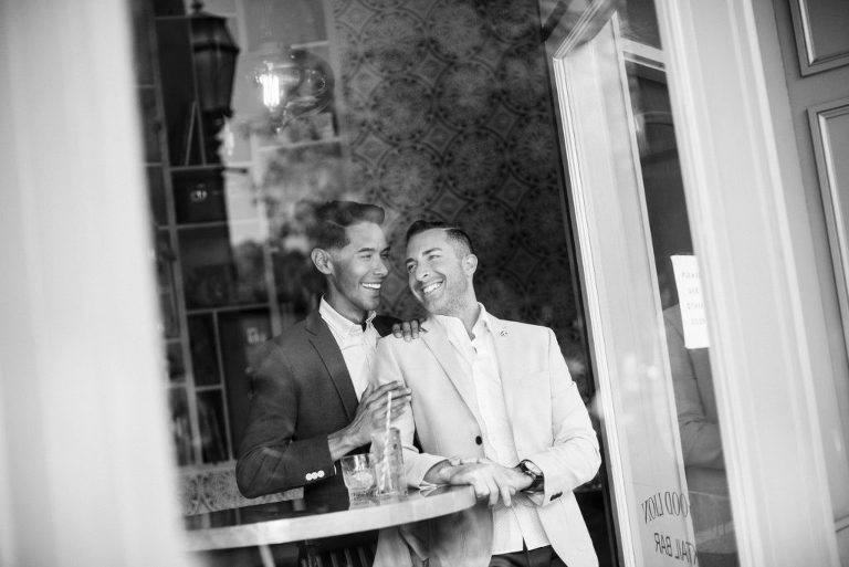 black and white photo of gay couple laughing through a window of a bar in Santa Barbara