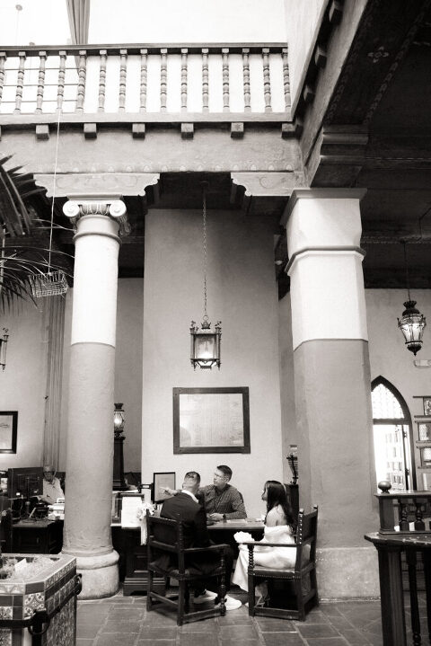 Bride and groom sitting at desk of county clerk in Santa Barbara Courthouse Hall of Records