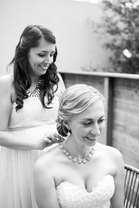 bridesmaids putting diamond necklace on bride