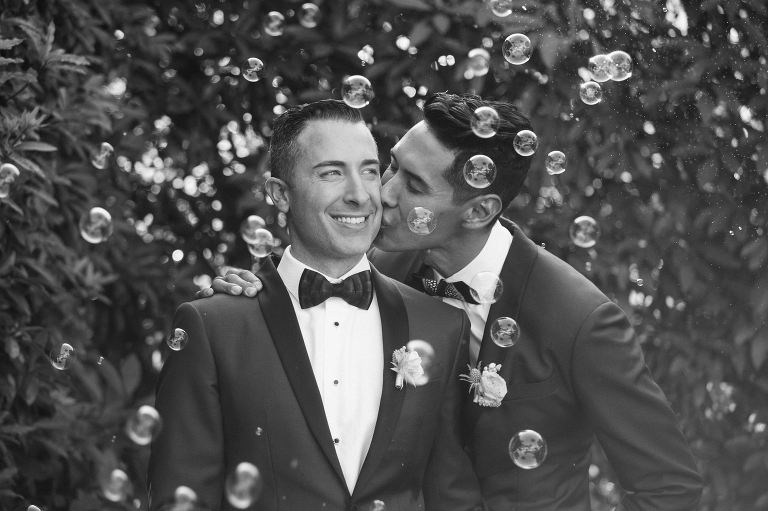 Two grooms hugging in the middle offloading bubbles.