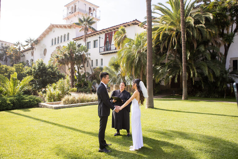 Bride and groom getting married outside by Santa barbara Courthouse county clerk with courthouse building in background