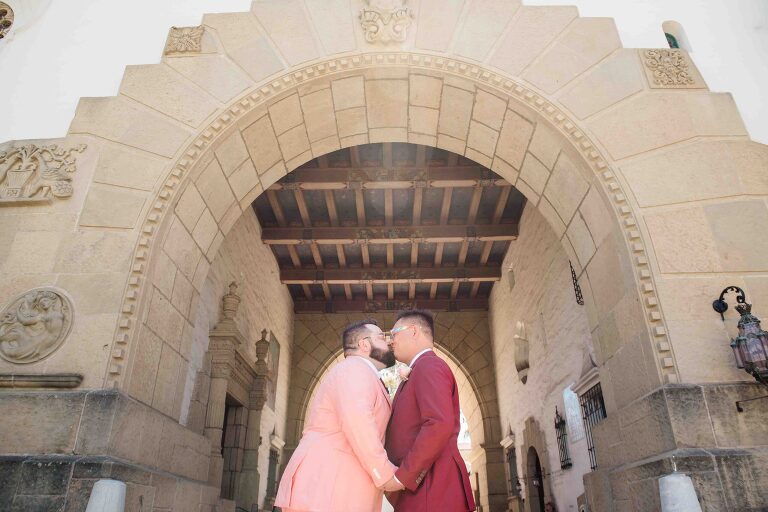 Gay couple kissing in from of archway of santa barbara courthouse