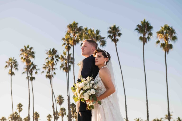 bride and groom at east beach in santa barbara with palm trees behind them looking out towards the ocean