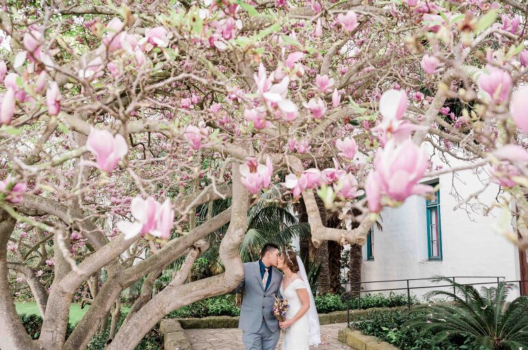 Bride and groom kissing under pink blooms at santa barbara courthouse